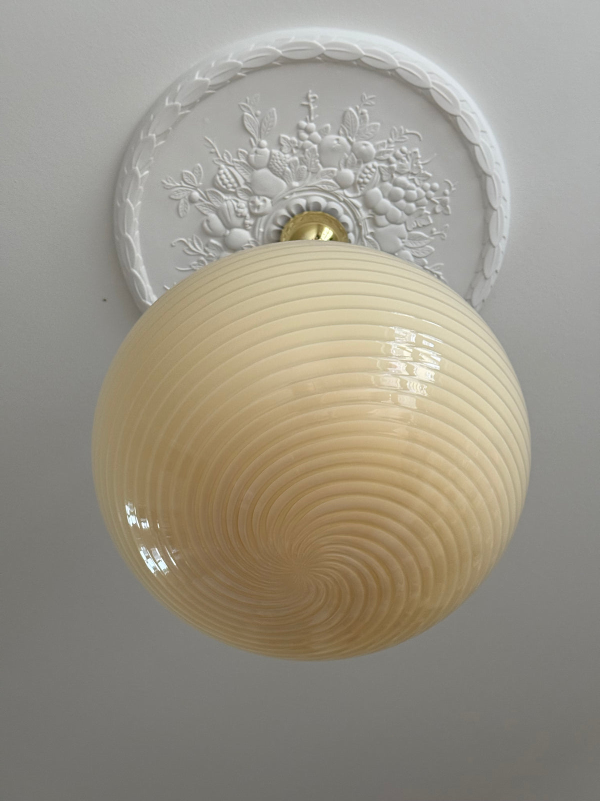 Tændt gul vintage Murano pendel med swirl-mønster under en hvid loftsroset